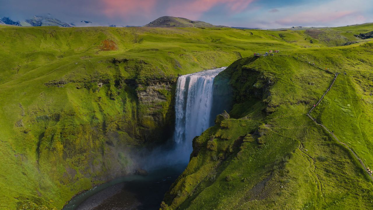 Aerial view of Skógafoss dropping off a green cliff, with the old coastline plateau behind it