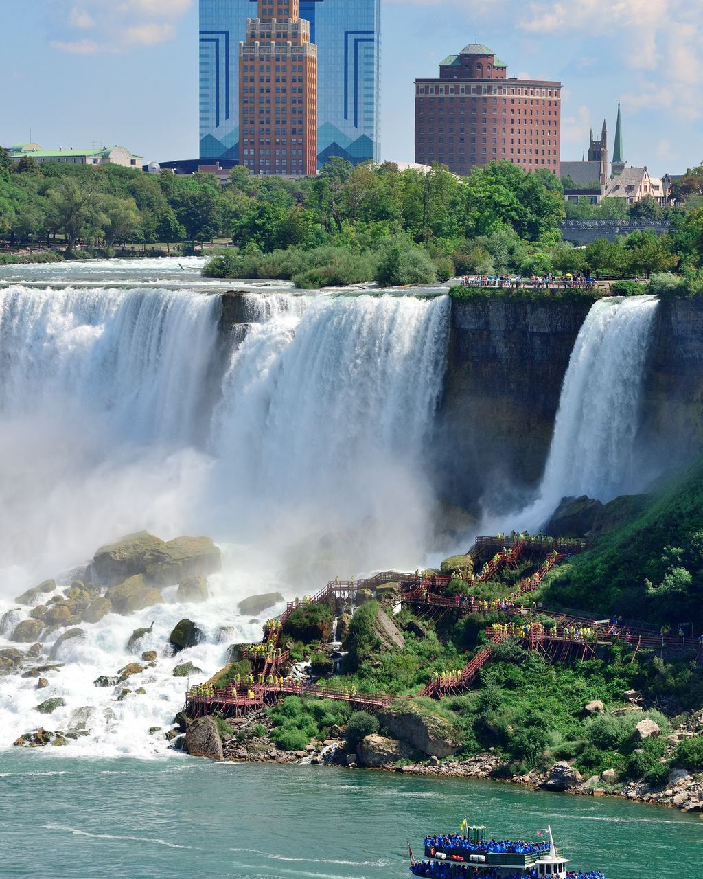The American Falls at Niagara with rock blocks piled at the foot, a smaller fall at right and a tour boat in the river