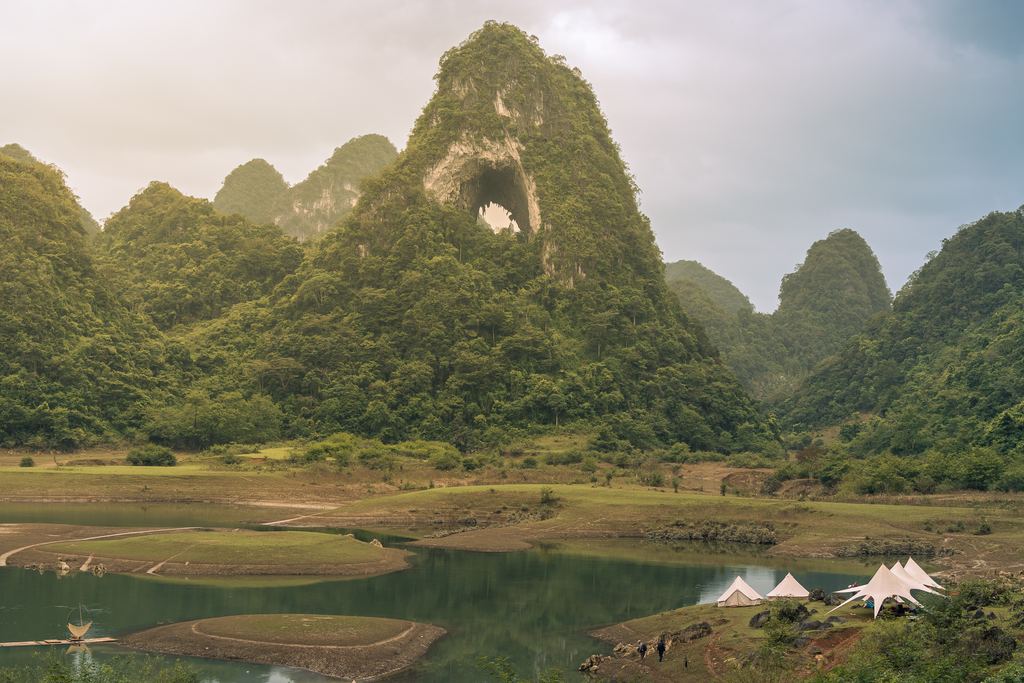 Angel Eye Mountain in Cao Bang, a green peak with a round hole near the top, and tents by a lake