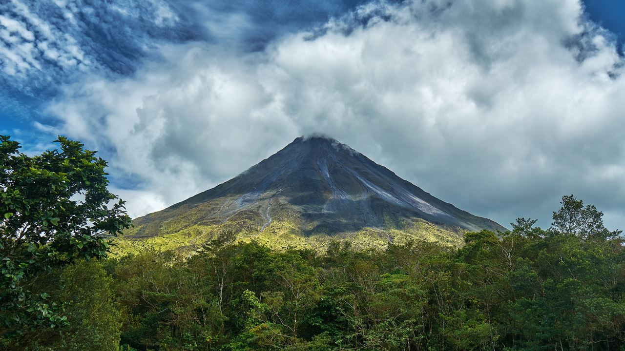 Arenal volcano, a dark cone under clouds, rises above green forest near La Fortuna, Costa Rica
