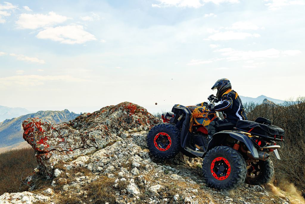 Rider in a helmet on an ATV at a rocky ridge with mountains behind
