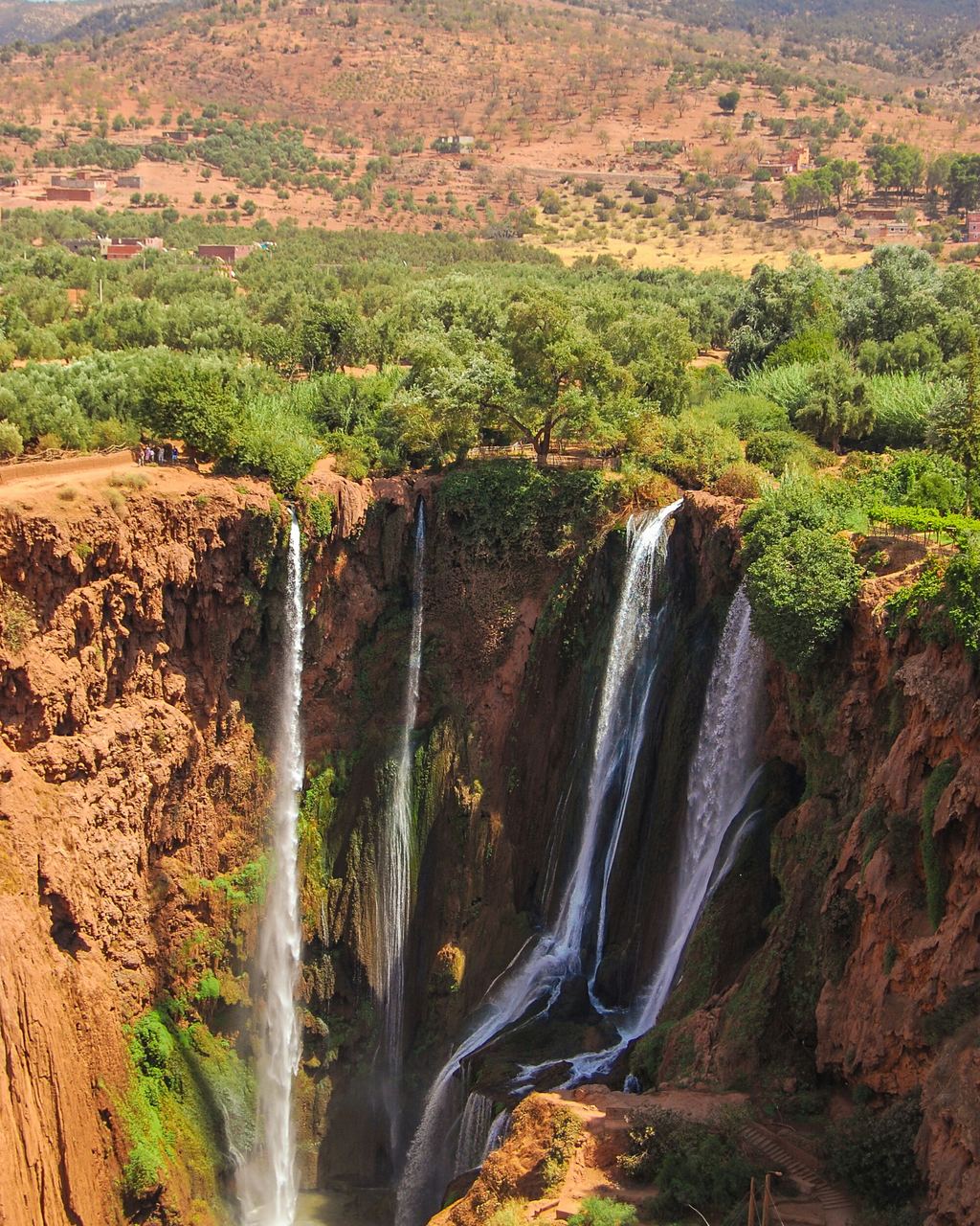 Ouzoud waterfall tumbling down a mossy cliff to a pool with cafe tables at the foot