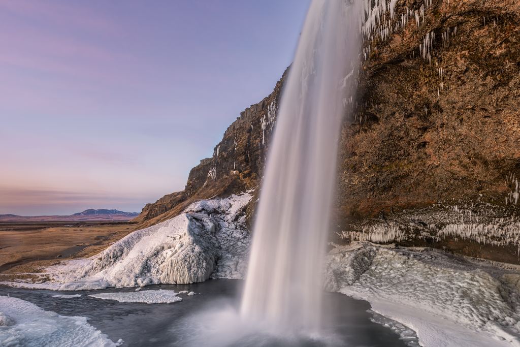 Seljalandsfoss seen from the path behind the water, with ice on the ground
