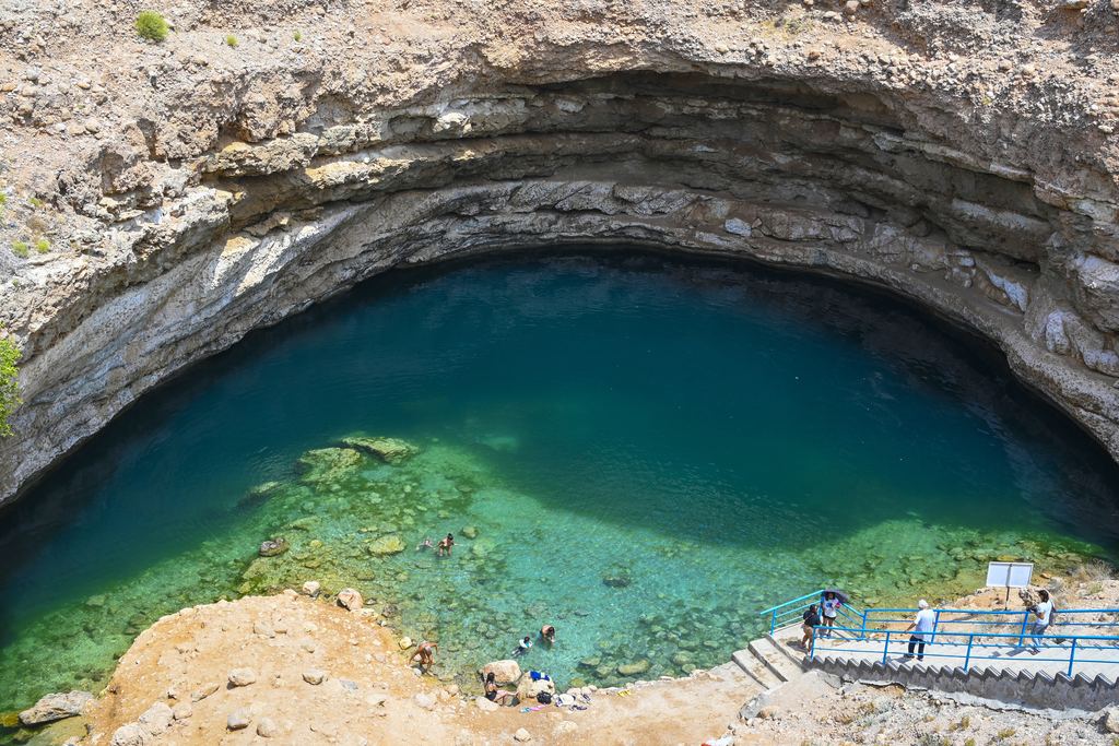 Bimmah Sinkhole near Muscat, Oman, with its stairway and swimmers in turquoise water