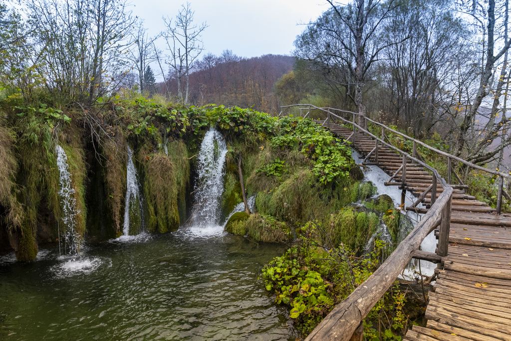 Wooden boardwalk beside small waterfalls and a green lake at Plitvice Lakes National Park, Croatia