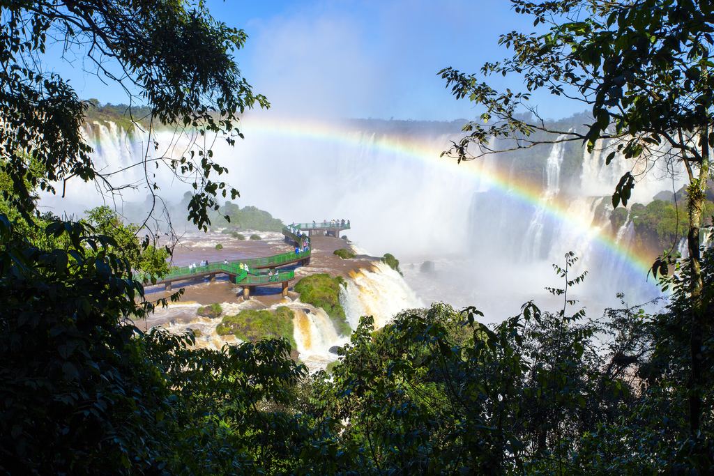 Green catwalk over the river on the Brazilian side of Iguazu Falls with a rainbow in the mist
