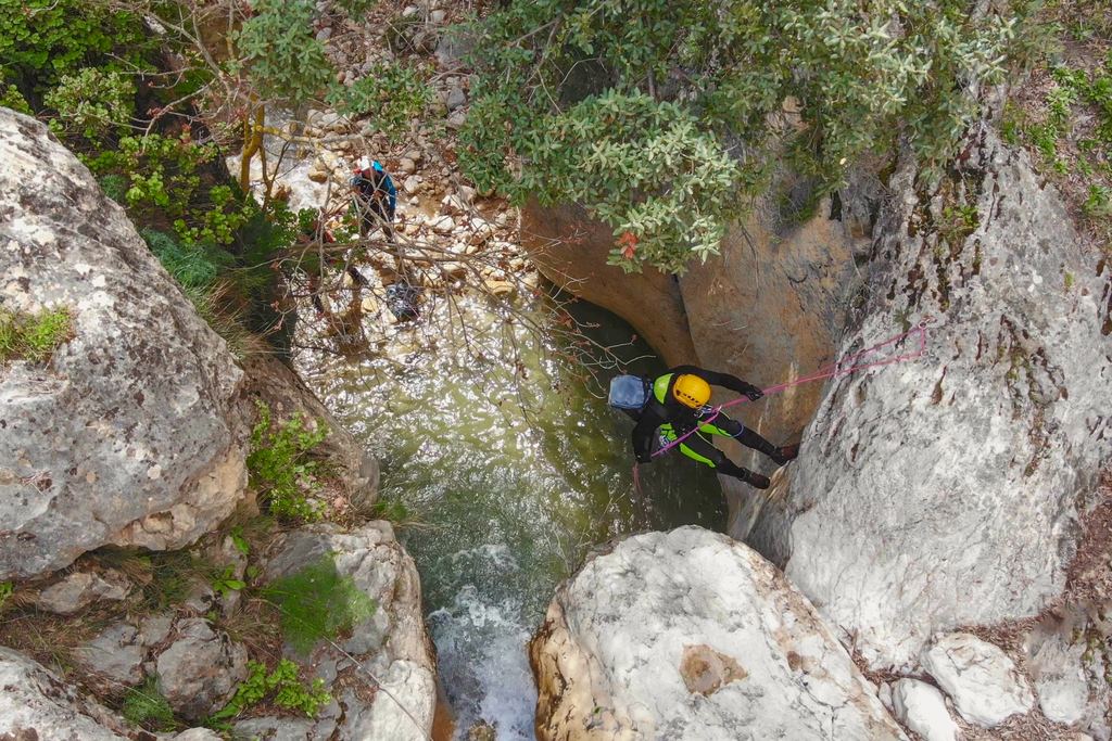 A canyoner in helmet and harness rappelling down a rock wall into a green pool