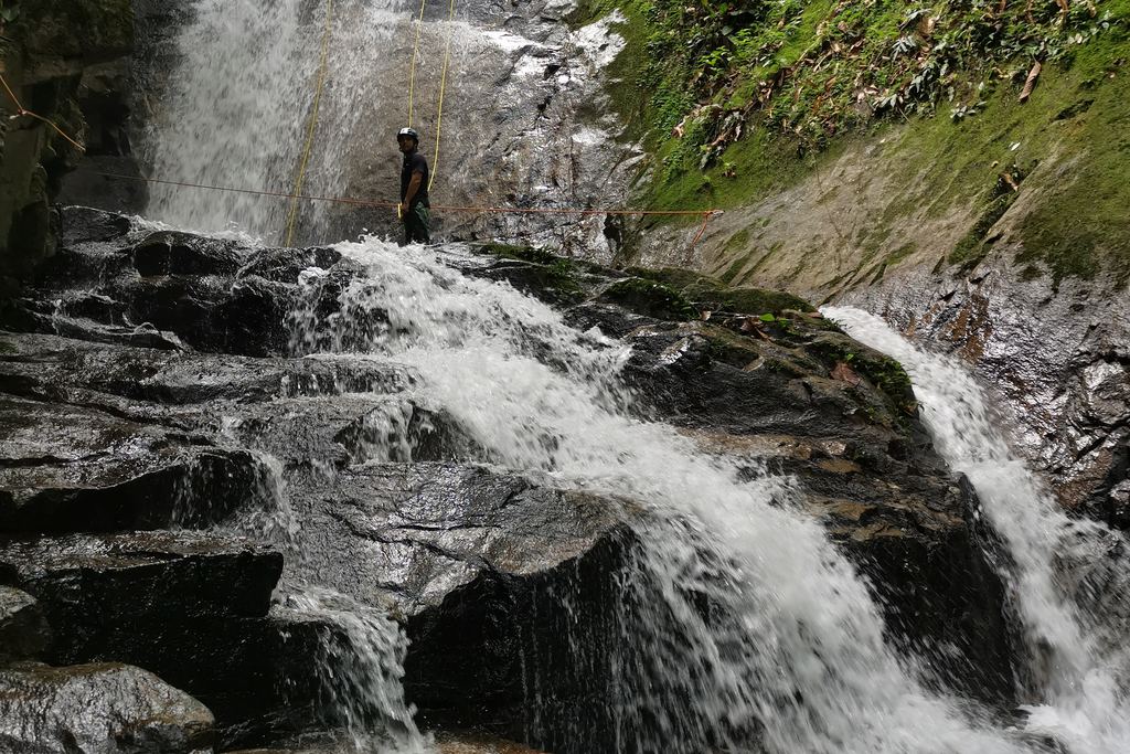 Canyoners abseiling down a waterfall between dark rocks in a tropical forest
