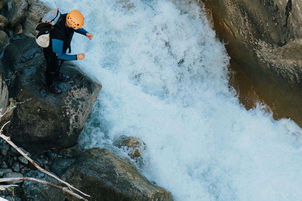 Two canyoners in helmets descending a waterfall in a rocky gorge