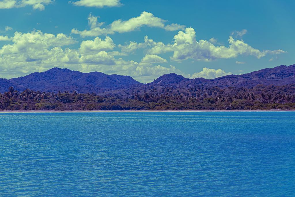 Calm blue sea in front of a palm-lined shore and blue mountains near Amber Cove, Puerto Plata province