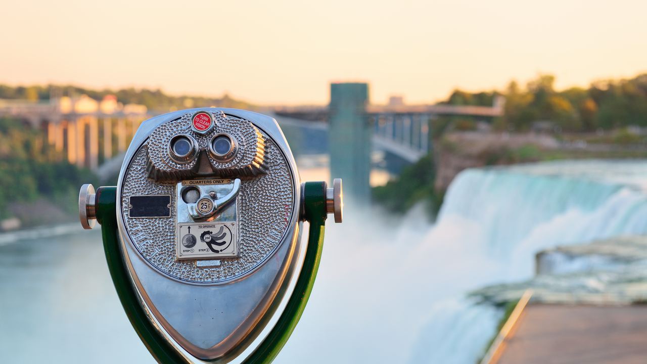 Coin-operated viewer at an overlook above the American Falls at Niagara, with a bridge blurred behind