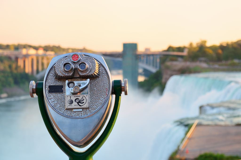 Coin-operated viewer at an overlook above the American Falls at Niagara, with a bridge blurred behind