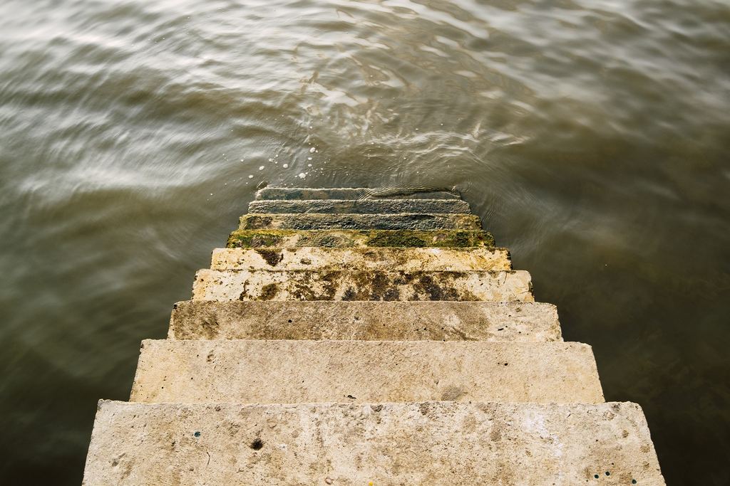 Concrete steps with moss and algae descending into dark water seen from above