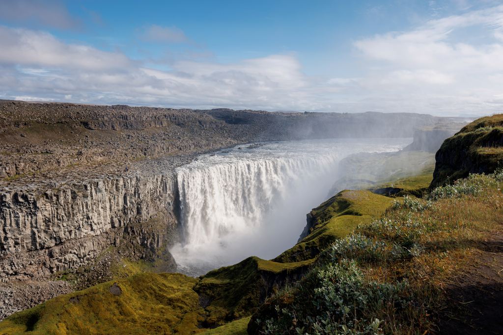 Dettifoss in northeast Iceland, a broad curtain of grey glacial water beside basalt columns in the canyon