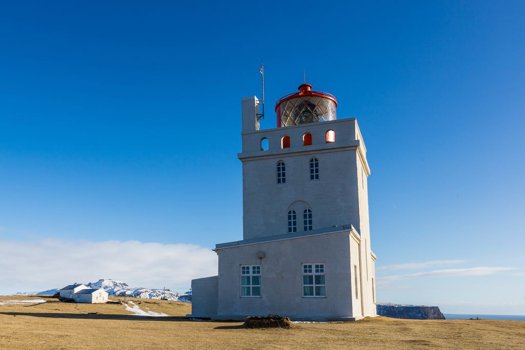 The white lighthouse on the Dyrhólaey promontory under a blue sky
