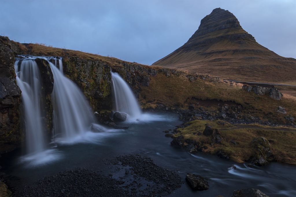 Three small falls over a mossy ledge below a pointed mountain in Iceland