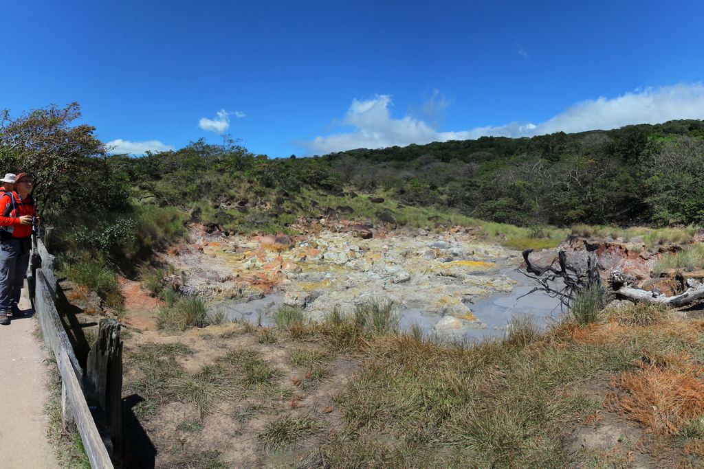 Hikers on a fenced path above a field of steaming vents and mud in Rincón de la Vieja National Park