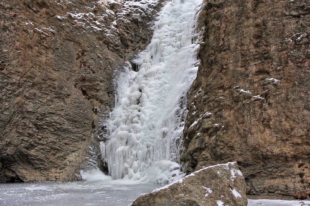 A frozen waterfall between dark rock walls with snow on the ground