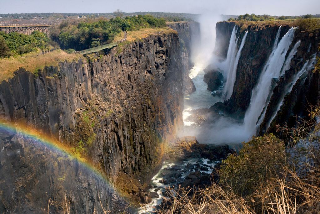The Victoria Falls gorge with a rainbow, a fall on the right and the bridge in the distance at the top left