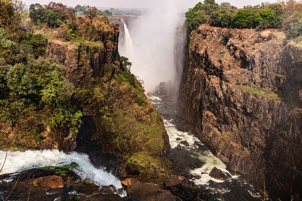 Basalt gorge walls with mist and a distant fall at Victoria Falls, seen from a viewpoint on the rim