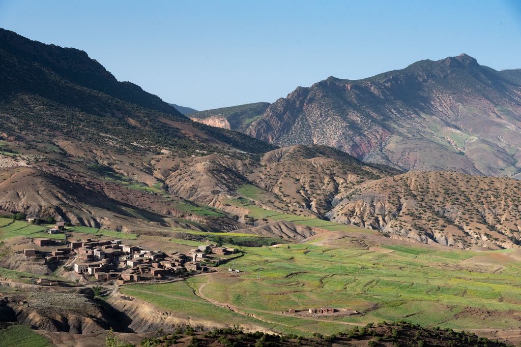 Berber village in a green valley floor beneath bare mountains in Morocco's Atlas