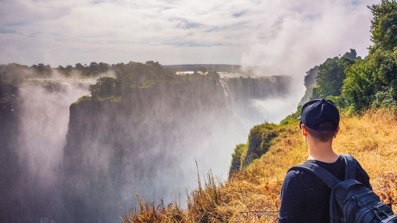 Hiker with a backpack looking at the spray rising from the Victoria Falls gorge in Zimbabwe