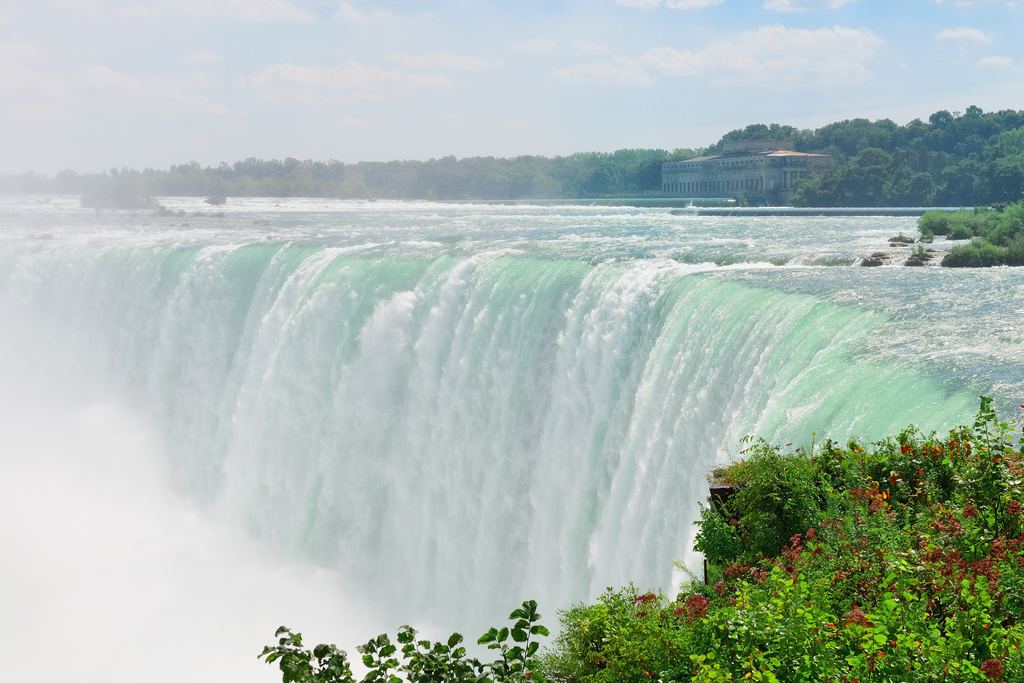 Green water curving over the crest of the Horseshoe Falls at Niagara with trees in the foreground