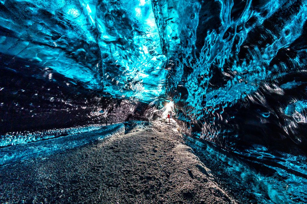A walker in a glacier ice cave with blue ice walls and ceiling