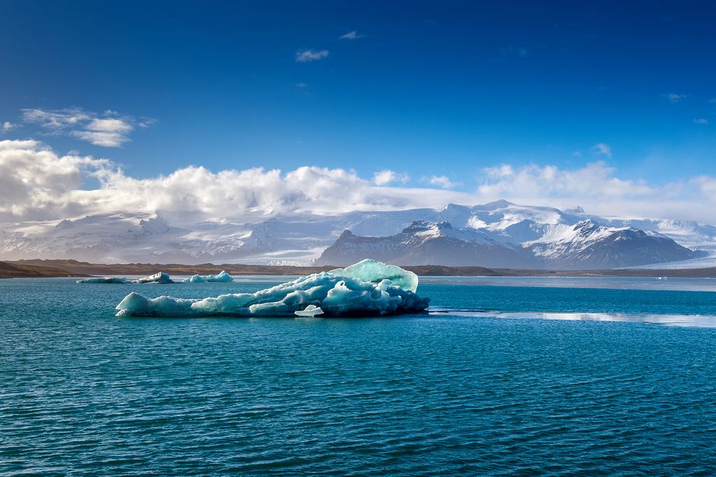 A blue iceberg floating in Jökulsárlón with snow-covered mountains behind