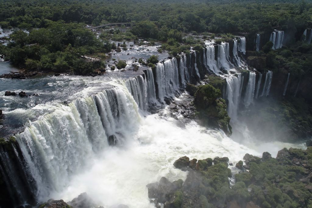 Iguazu Falls seen from above in high water, with brown river water below a long curtain of waterfalls
