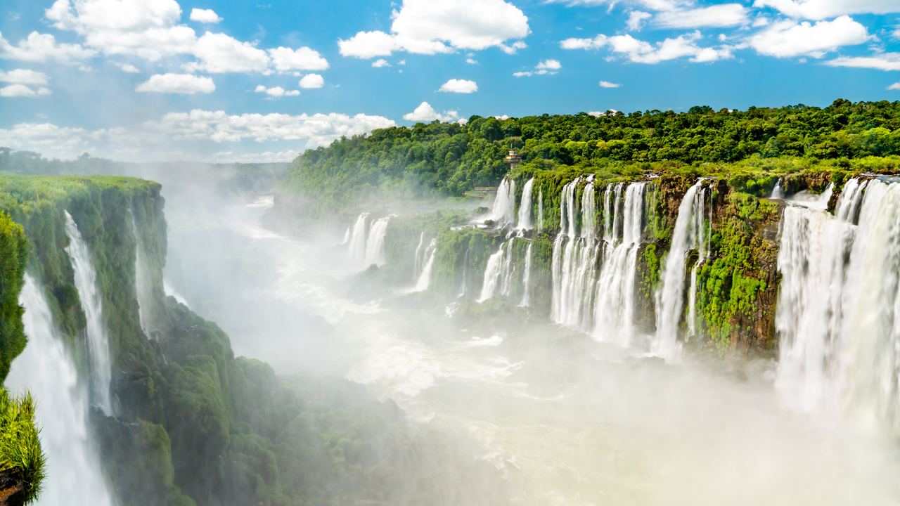 Mist rising over the Iguazu Falls with several cascades and green forest along the gorge