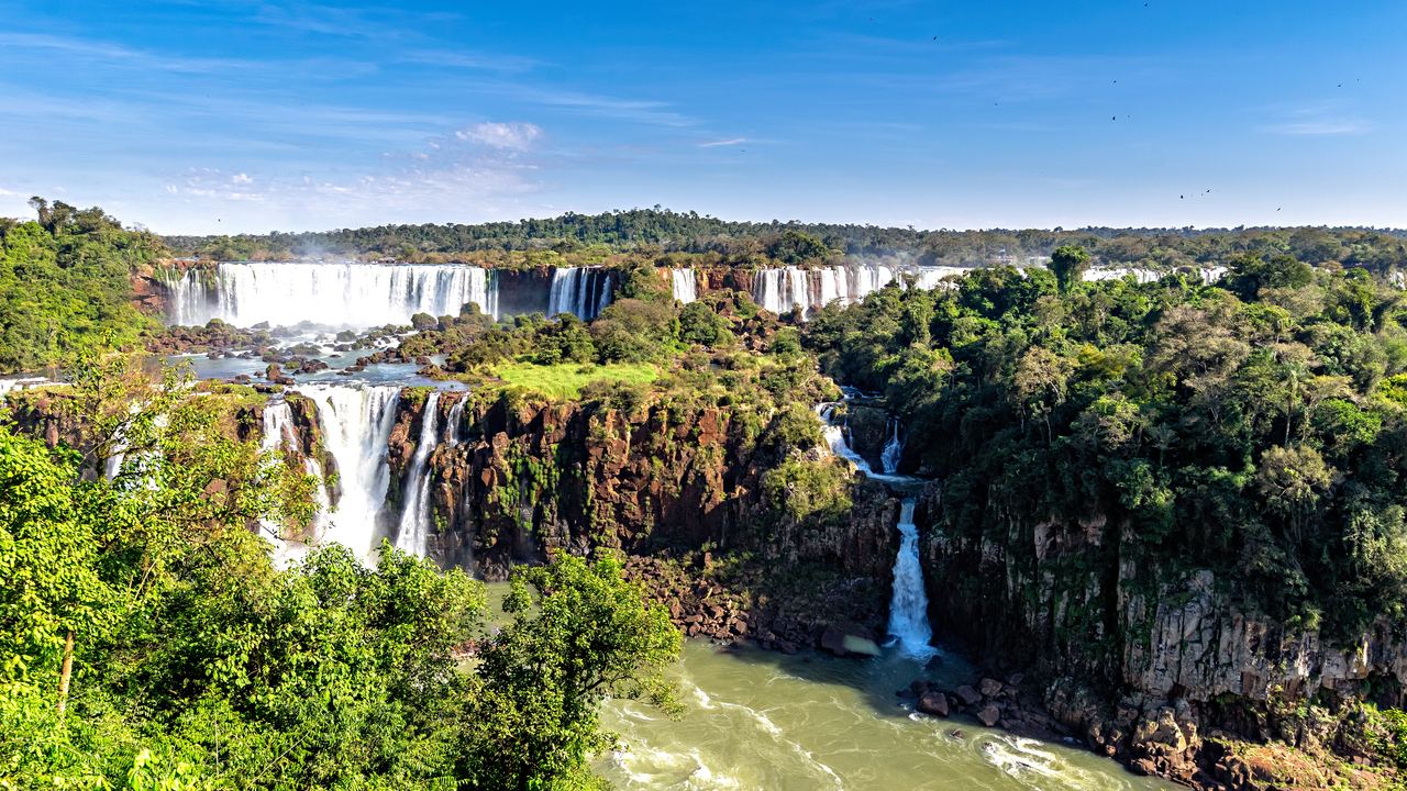 Iguazu Falls seen from above, with falls along a basalt cliff and a green river below