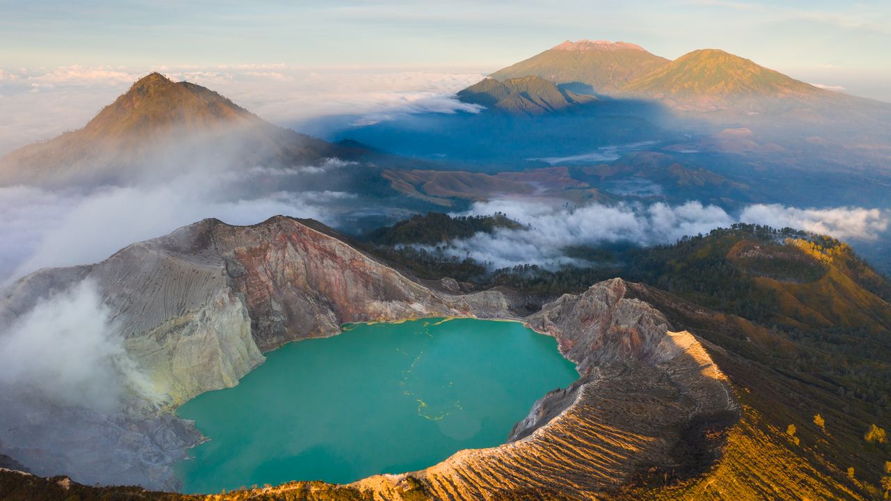 Turquoise acid lake in the Ijen crater at sunrise with volcanoes rising behind it in East Java