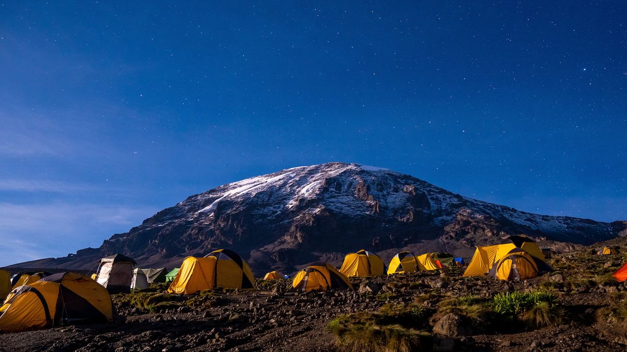 Mount Kilimanjaro with snow on its summit above yellow tents under a starry sky in Tanzania