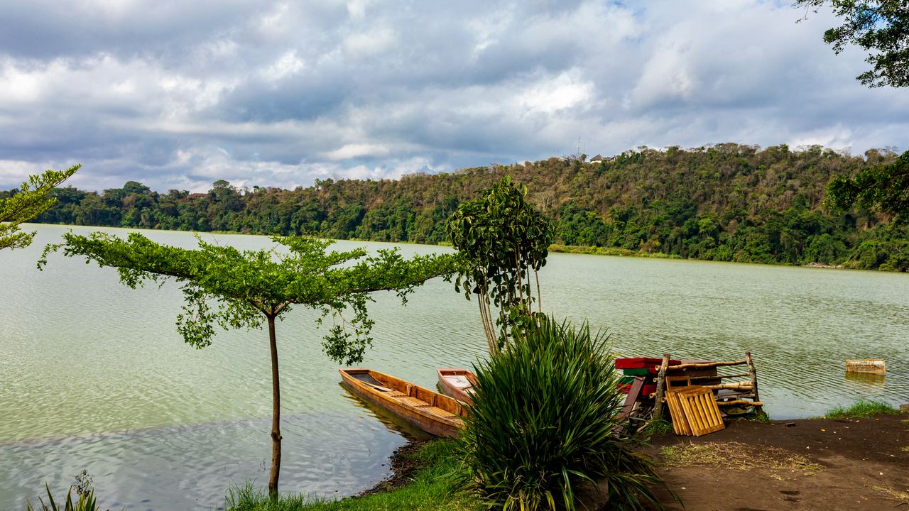 Boats on the green water of Lake Duluti, a volcanic crater lake near Arusha, with forested slopes beyond