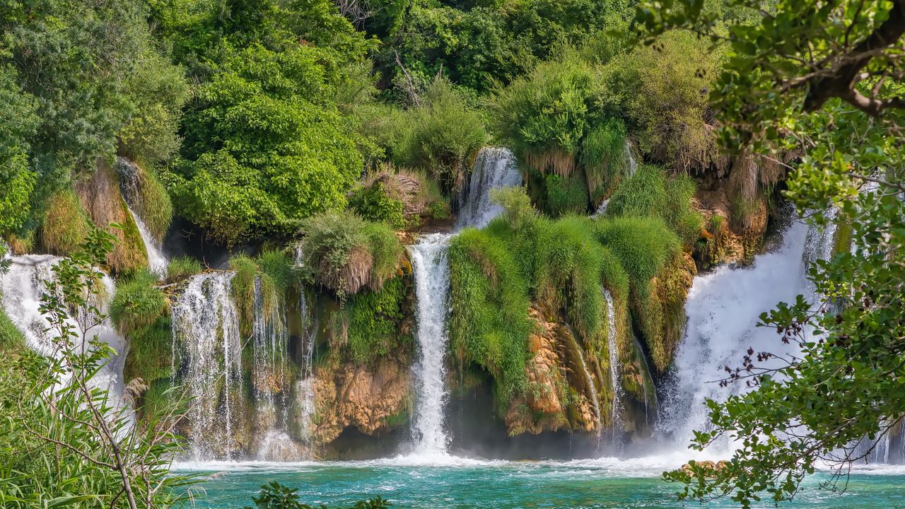Several waterfalls tumbling over green tufa ledges into a turquoise pool in Krka National Park, Croatia