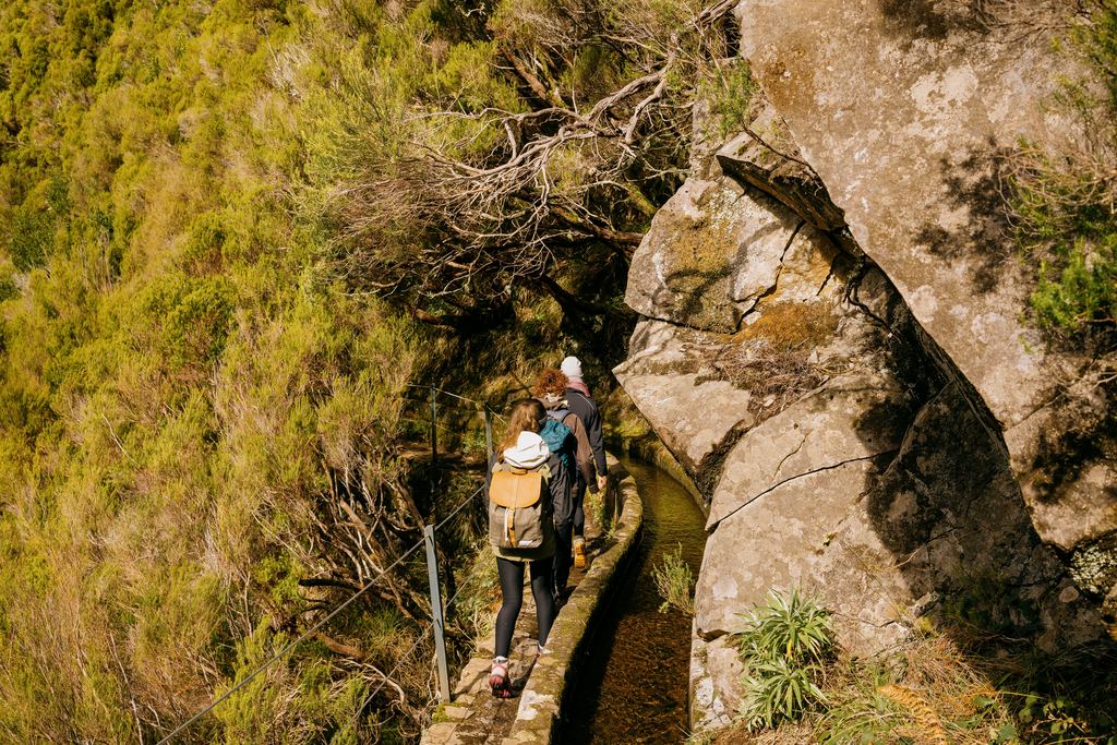 Walkers on a narrow levada path above a forested slope on Madeira