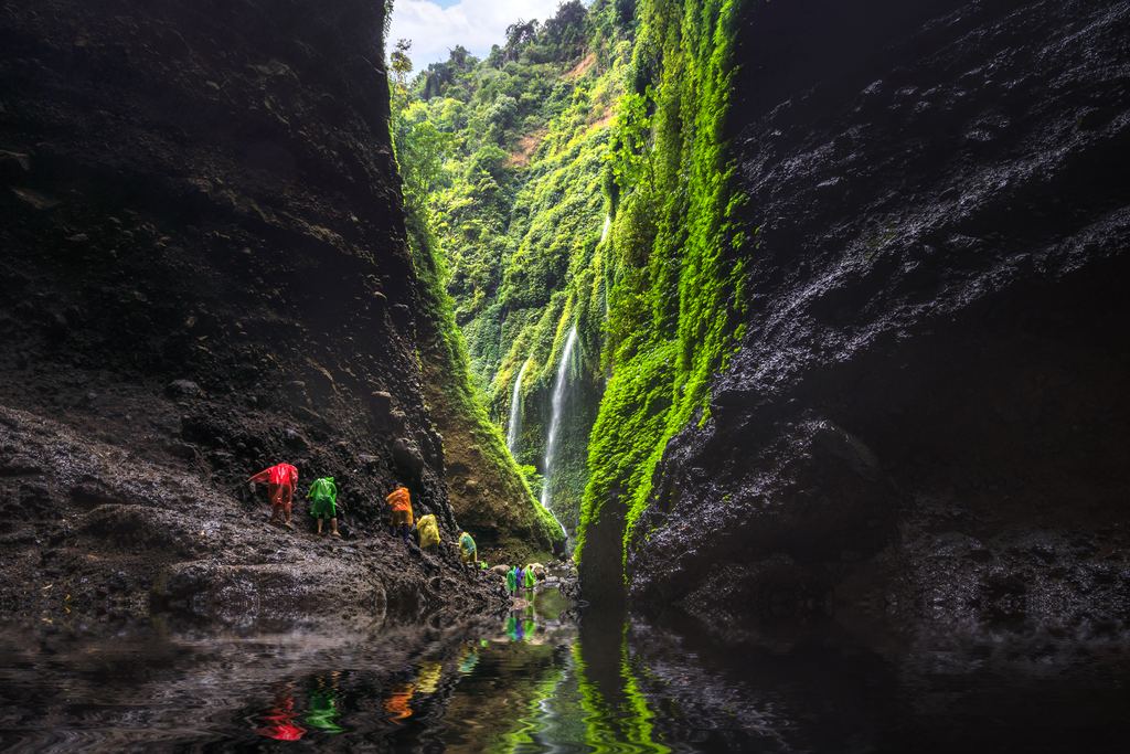 Visitors in rain ponchos walking into the mossy Madakaripura gorge in East Java, Indonesia