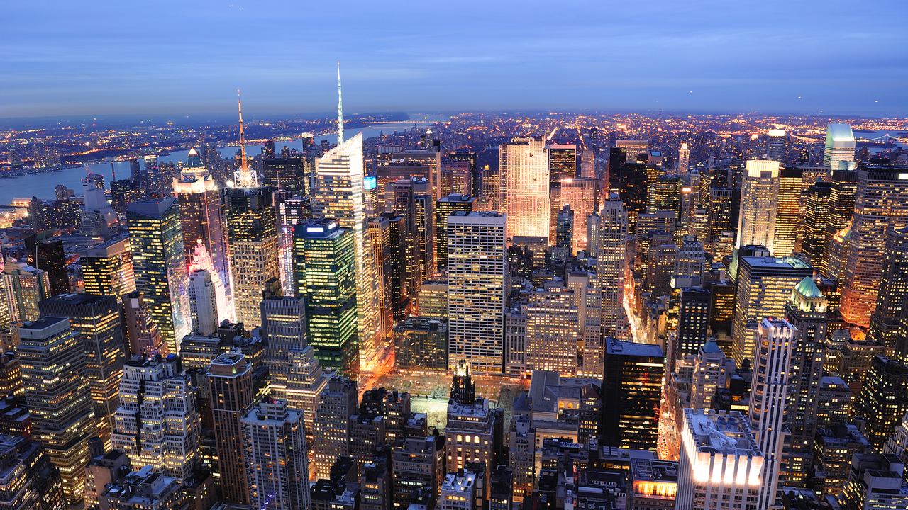 Manhattan skyline at dusk seen from above with lit skyscrapers and the Hudson River