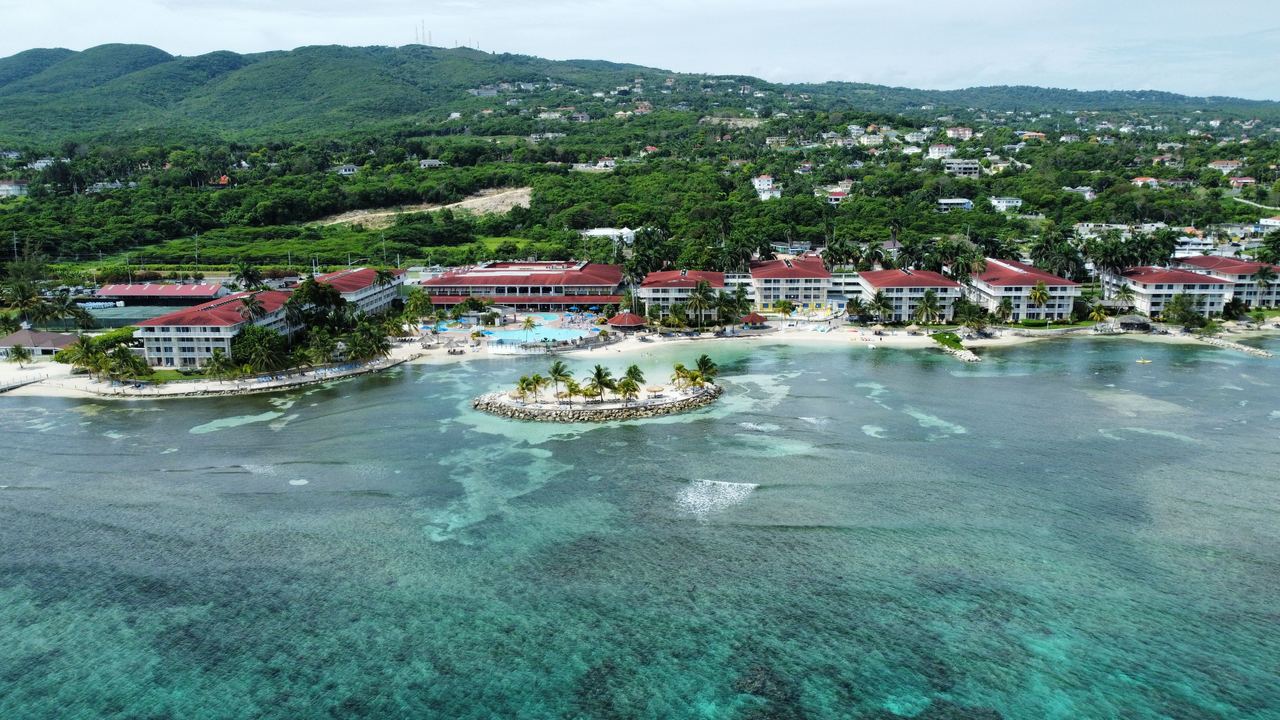 Resorts along a beach and turquoise reef water below green hills at Montego Bay, Jamaica