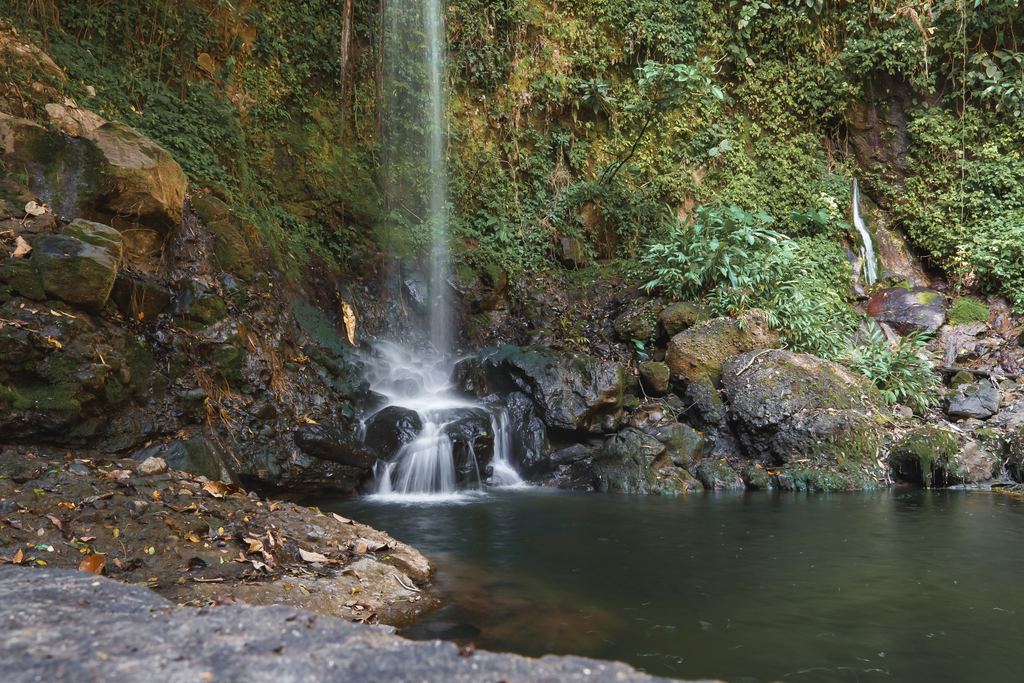 A thin waterfall falls onto mossy rocks into a still pool in the forest at Montezuma, Nicoya Peninsula, Costa Rica