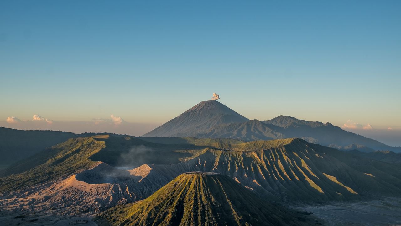 Mount Bromo and its crater at dawn with Mount Semeru and a plume of smoke behind