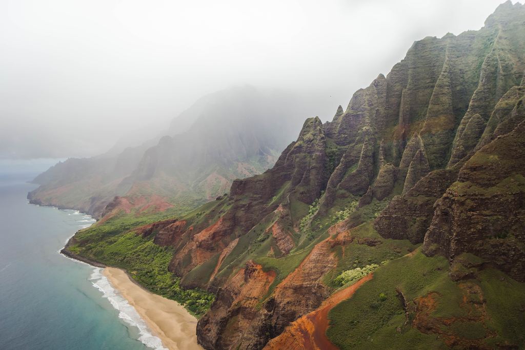Steep green cliffs of the Napali Coast on Kauai above a sandy beach in haze