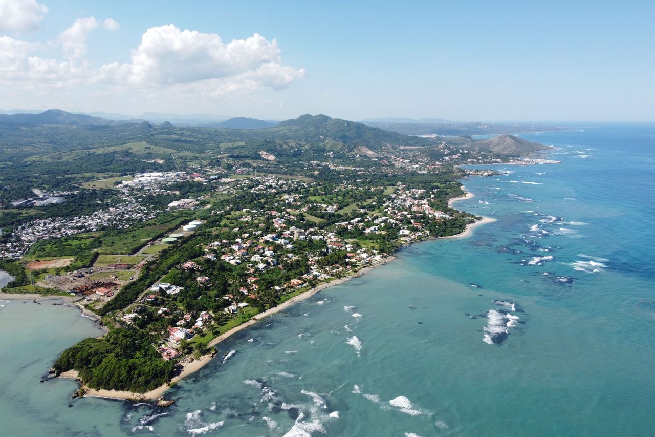 Aerial view of a green headland with houses, a golf course and surf on the north coast of the Dominican Republic