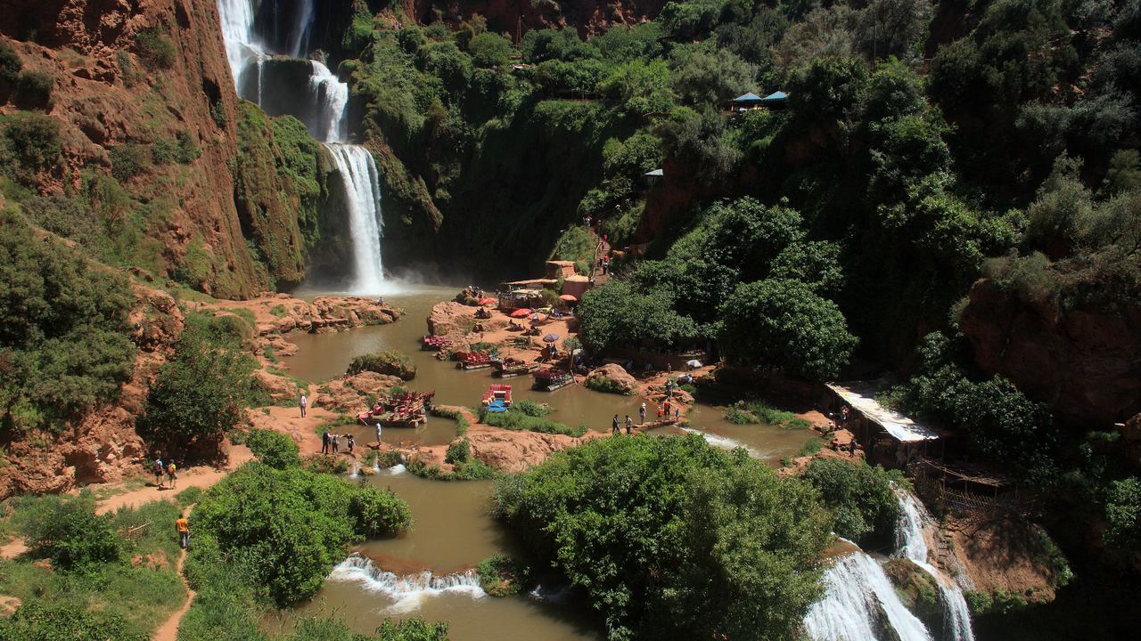 Ouzoud waterfalls above a brown pool with boats and visitors, framed by green slopes, Morocco