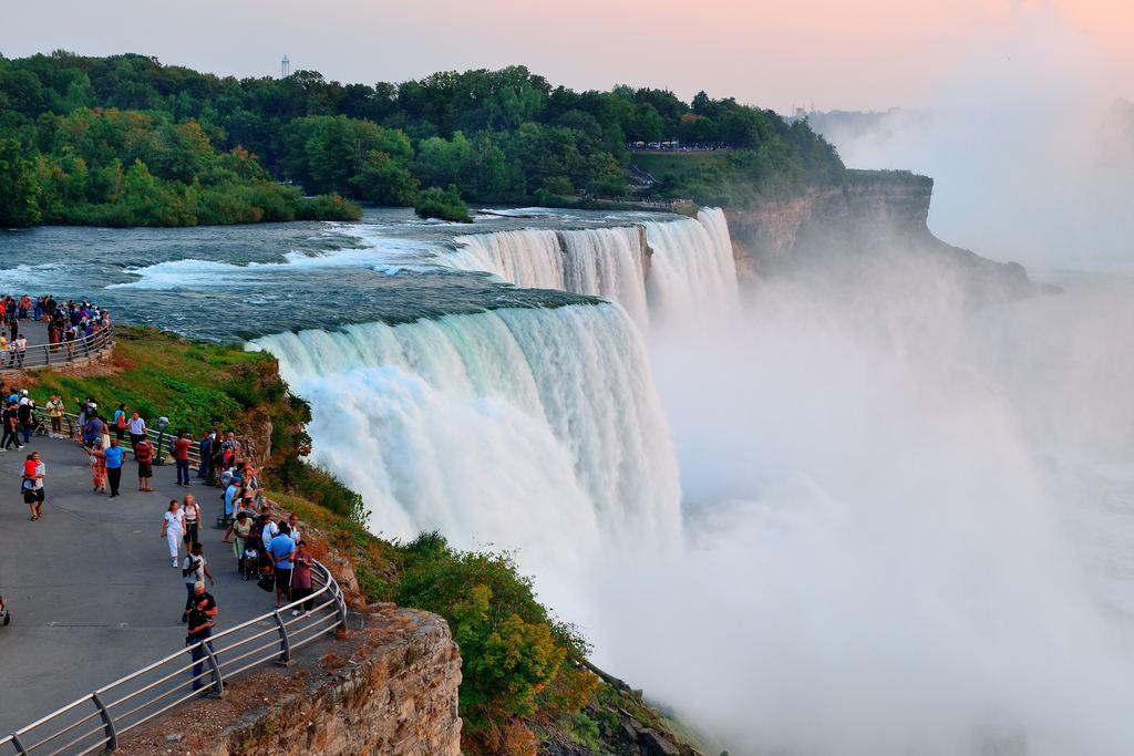 Visitors at a railing above Niagara Falls in late evening light
