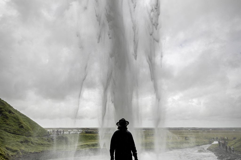 Person seen from behind standing in a rock alcove behind a curtain of falling water