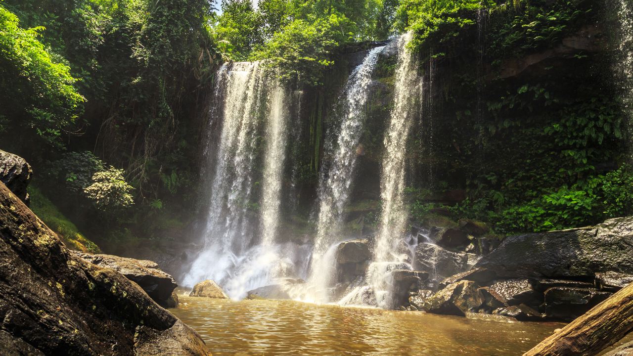 Phnom Kulen waterfall falling in several strands into a brown pool, framed by jungle and rocks