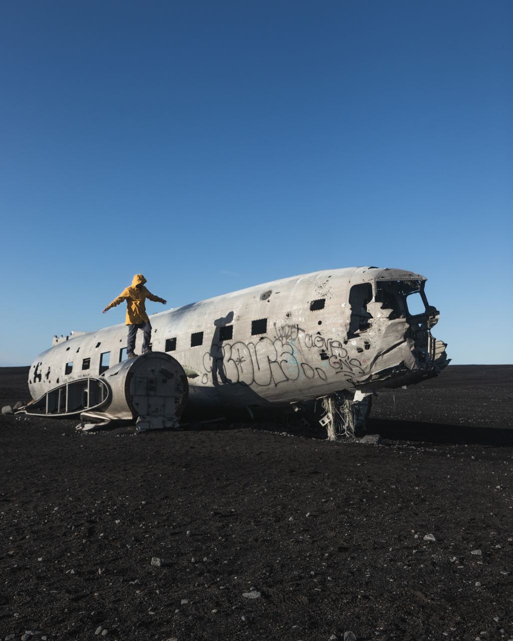 A visitor standing on the fuselage of the abandoned DC-3 on the black sand plain