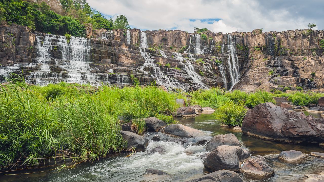 Pongour Falls near Da Lat, a wide rock face with water running down it above a grassy riverbank